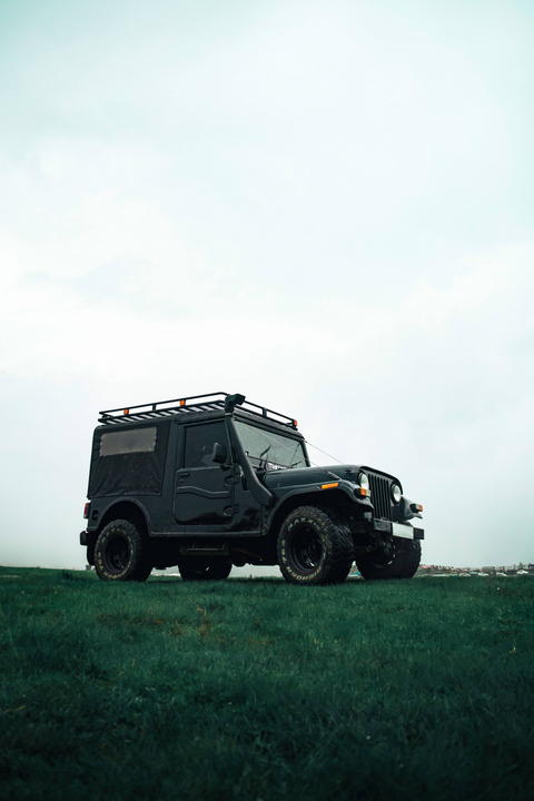 Free photo of black mahindra thar parked in a field with a sky background
