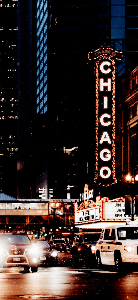 cars driving down a city street at night with a chicago sign