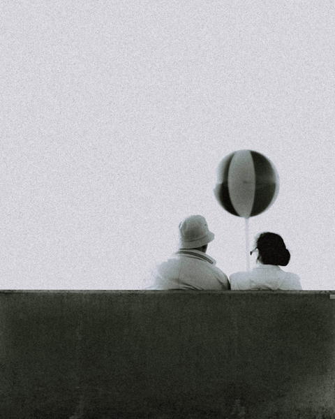 Free photo of couple sitting on a bench watching a balloon fly through the air