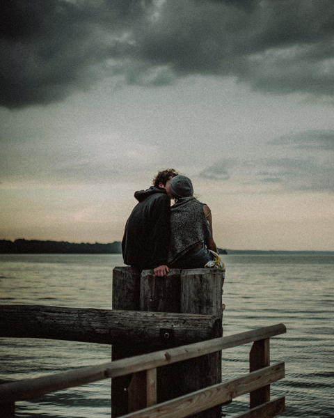 Free photo of couple sitting on a wooden pier looking out at the water