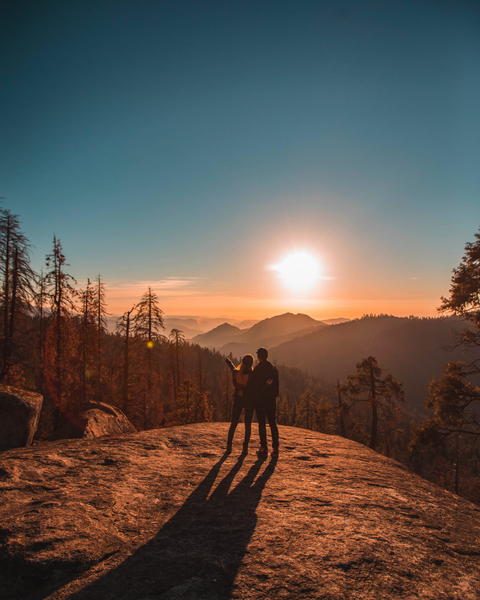 Free photo of couple standing on a rock with the sun setting in the background