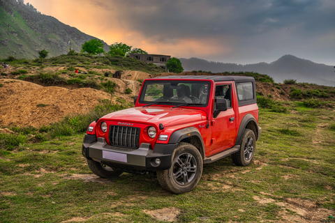 Free photo of Mahindra Thar parked on a grassy hill with a mountain in the background