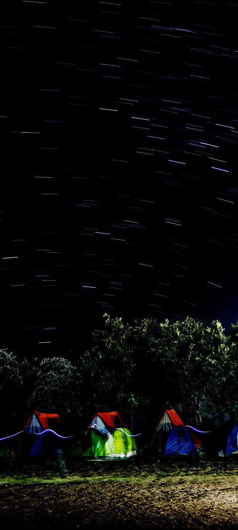 nighttime time picture of a group of tents with a star trail in the sky