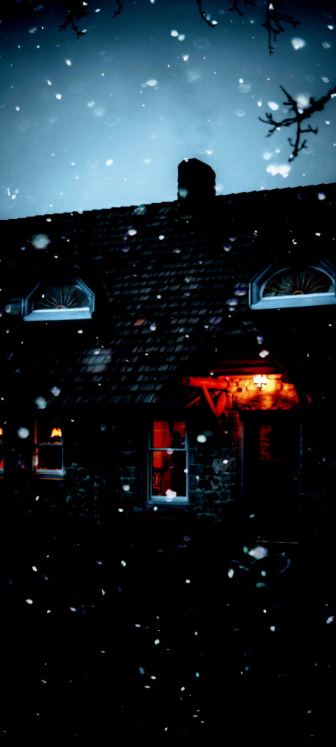 snowy night scene of a house with a red light in the window