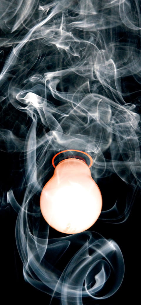 smoke swirling around a white light bulb on a black background
