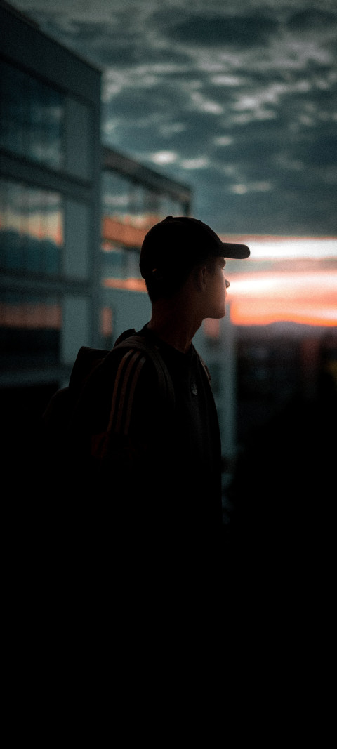 man in a cap and backpack looking out at the sunset