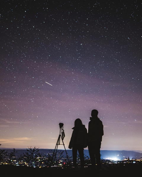 Free photo of starry night sky with silhouette of two people and a camera