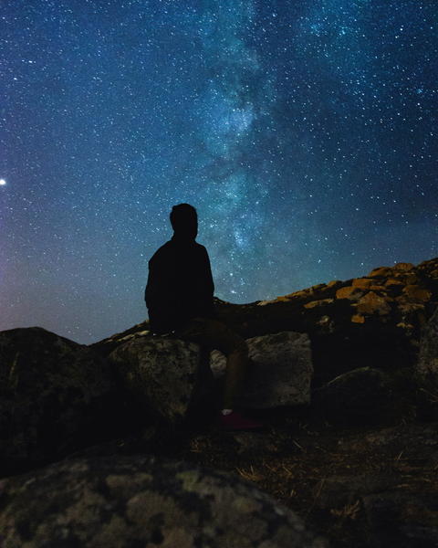 Free photo of starry sky with a person sitting on a rock looking at the stars