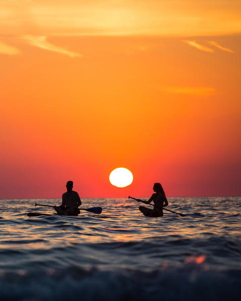 Free photo of surfers in the ocean at sunset with a bright orange sky