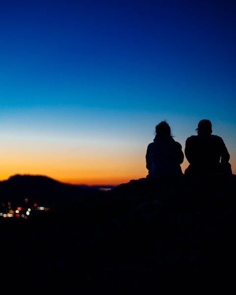 Free photo of two people sitting on a hill watching the sunset