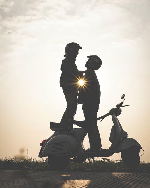 Free photo of two people standing on a scooter with the sun behind them