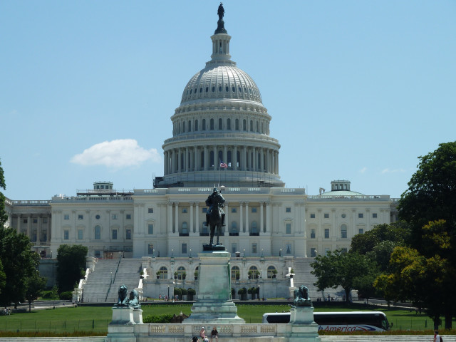 The United States Capitol Building, a neoclassical masterpiece, stands majestically against a clear blue sky. The iconic dome dominates the structure, surrounded by lush green lawns and statues. Located in Washington, D.C., the capital of the United States.