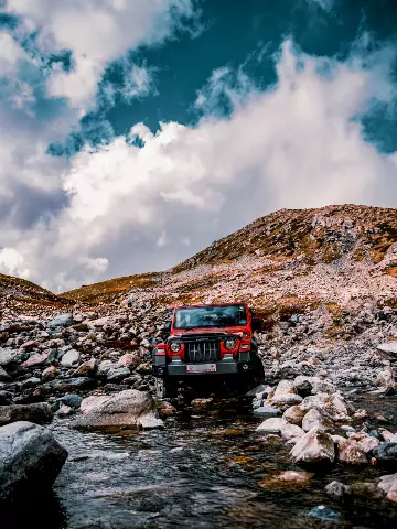 2020 Red Mahindra Thar driving through a rocky river in the mountains