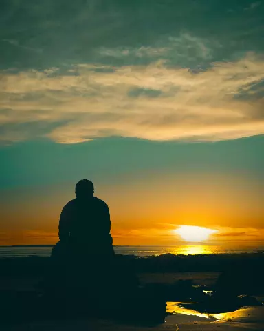 a man sitting on a rock watching the sunset
