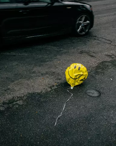 balloon with a smiley face drawn on it sitting on the side of the road