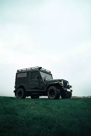 black mahindra thar parked in a field with a sky background