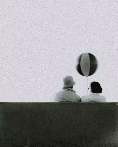 couple sitting on a bench watching a balloon fly through the air