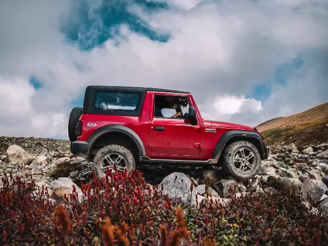 red Mahindra Thar driving on rocky terrain with cloudy sky