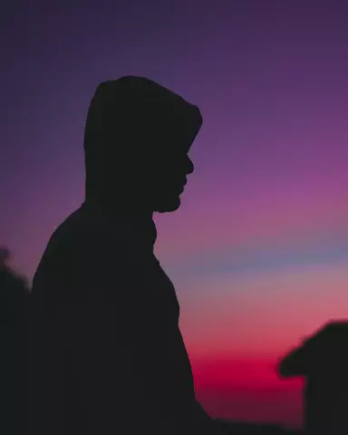 silhouette of a man in a cap and a shirt standing in front of a sunset