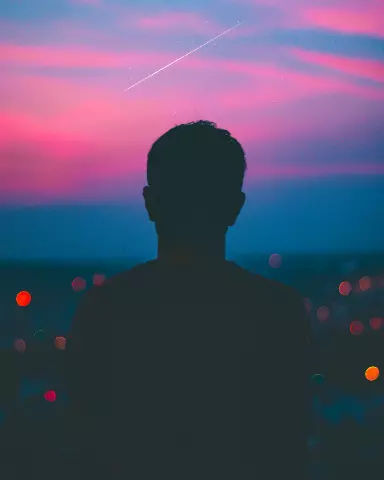 silhouette of a man standing in front of a city at sunset