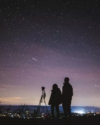starry night sky with silhouette of two people and a camera