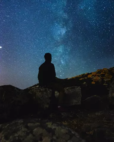 starry sky with a person sitting on a rock looking at the stars