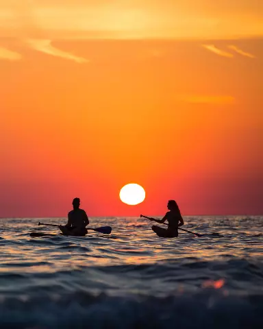 surfers in the ocean at sunset with a bright orange sky