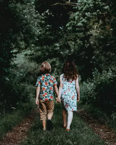 two children walking down a path in the woods holding hands