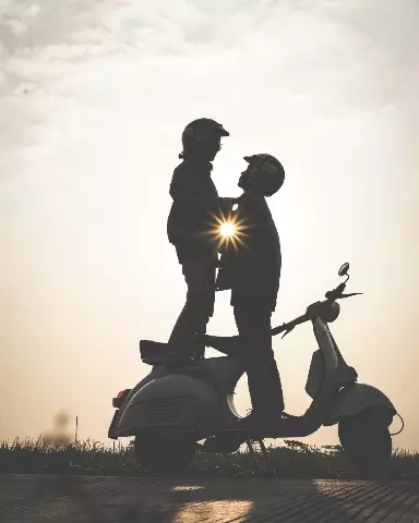 two people standing on a scooter with the sun behind them